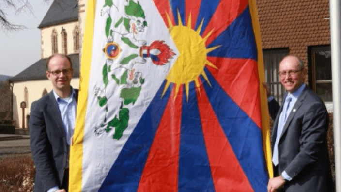 Michael Brand MdB (links) und Bürgermeister Jürgen Hahn hissen vor dem Rasdorfer Rathaus die Tibet-Flagge.